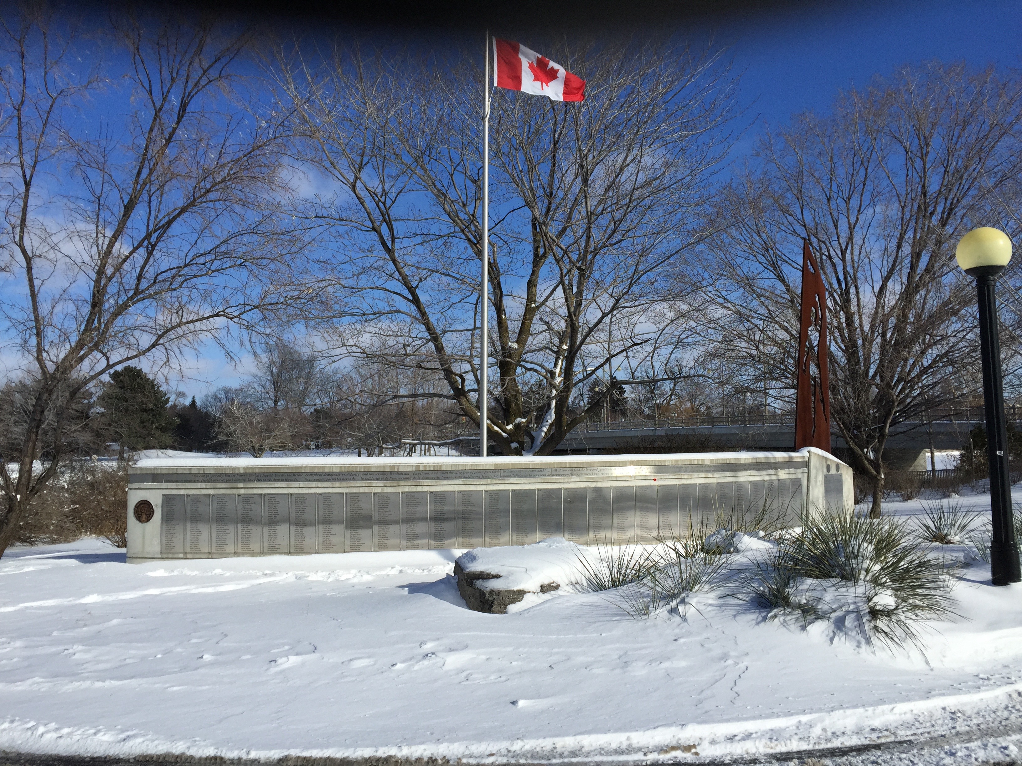 Photo of the Ottawa memorial. A long stone base holds plaques with names of Canadian volunteers. Behind the names stands a Canadian flag.