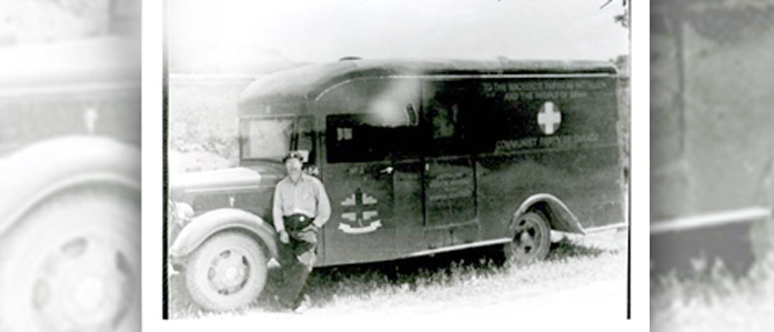 A black and white photograph of Walter Schuetrum standing in front of a Mackenzie Papineau Battalion ambulance. 